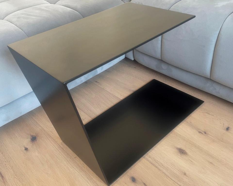 Couchtisch aus Metall, Farbe Scwharz. In Trapezform und U-Form der neben einem Sofa steht.
