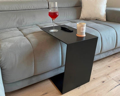 Couchtisch aus Metall, Farbe Scwharz. In Trapezform und U-Form der über ein Sofa geschoben wurde.