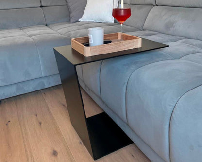 Couchtisch aus Metall, Farbe Scwharz. In Trapezform und U-Form der über ein Sofa geschoben wurde.