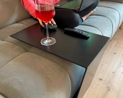 Couchtisch aus Metall, Farbe Scwharz. In Trapezform und U-Form der über ein Sofa geschoben wurde.