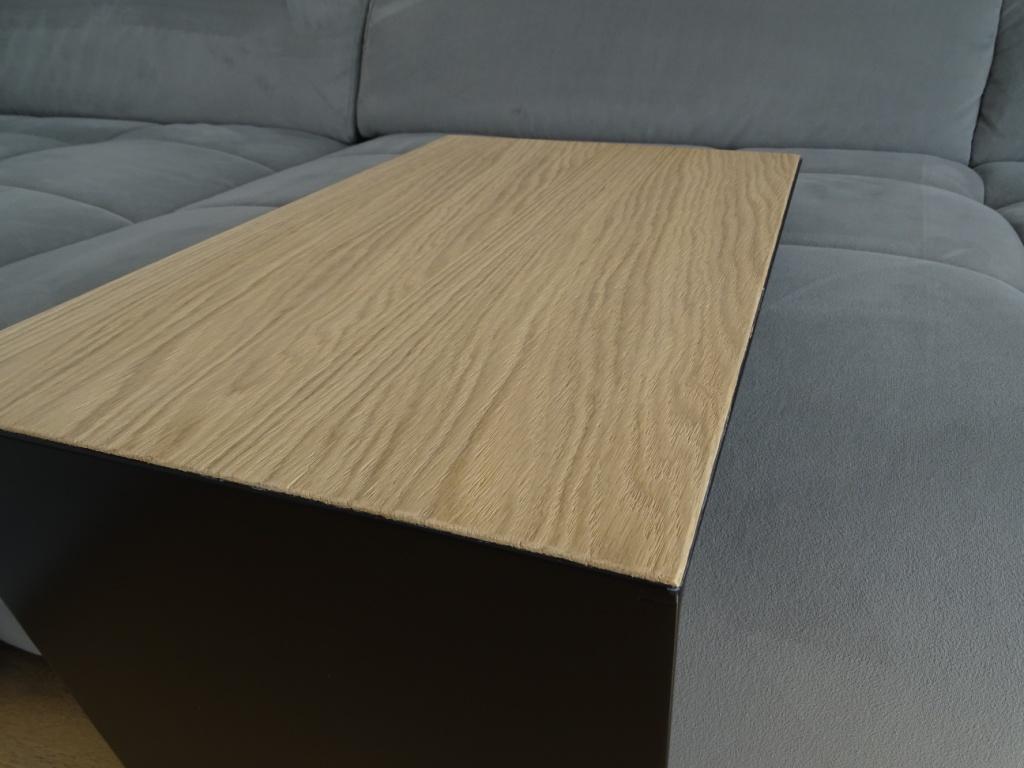 Couchtisch aus Metall, Farbe Scwharz und auf der Oberseite ist ein Eiche Furnier drauf geklebt. In Trapezform und U-Form der neben einem Sofa steht.