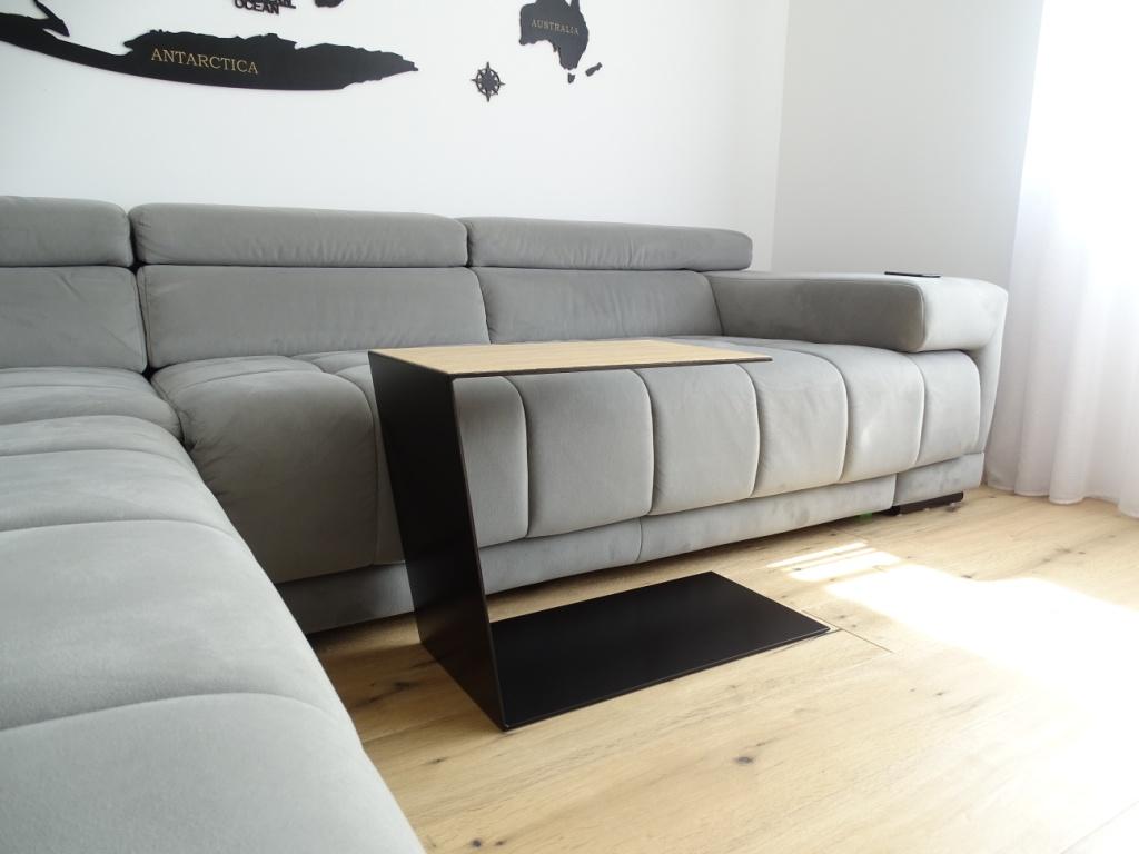 Couchtisch aus Metall, Farbe Scwharz und auf der Oberseite ist ein Eiche Furnier drauf geklebt. In Trapezform und U-Form der neben einem Sofa steht.