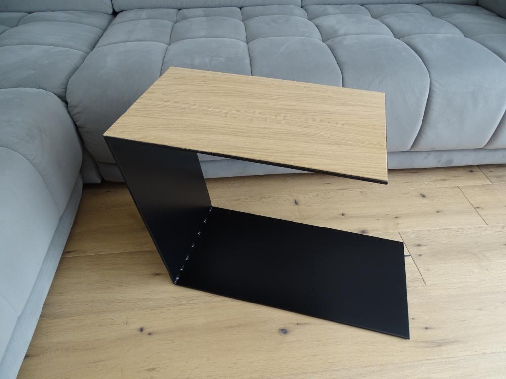 Couchtisch aus Metall, Farbe Scwharz und auf der Oberseite ist ein Eiche Furnier drauf geklebt. In Trapezform und U-Form der neben einem Sofa steht.