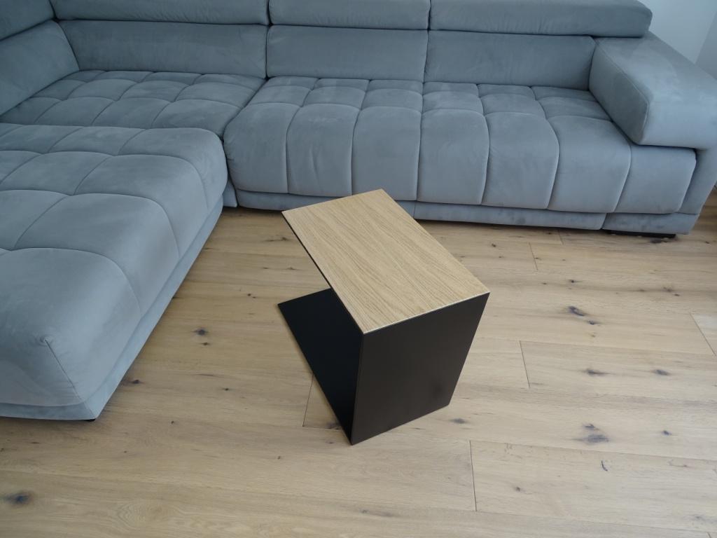 Couchtisch aus Metall, Farbe Scwharz und auf der Oberseite ist ein Eiche Furnier drauf geklebt. In Trapezform und U-Form der neben einem Sofa steht.