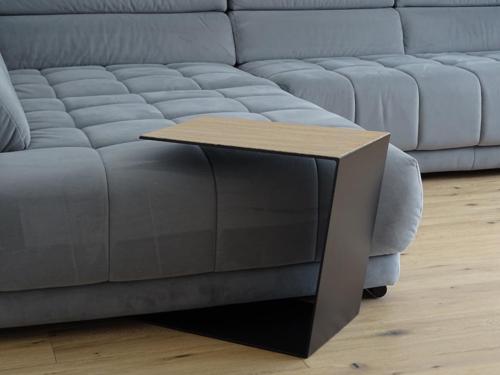 Couchtisch aus Metall, Farbe Scwharz und auf der Oberseite ist ein Eiche Furnier drauf geklebt. In Trapezform und U-Form der über ein Sofa geschoben ist.